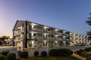 Un motel de varios pisos con una oficina central, varios balcones y un área de estacionamiento.