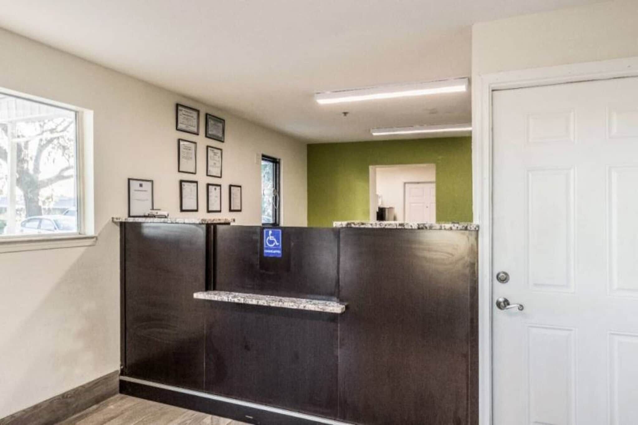 A reception area with a counter, framed certificates on the wall, a wheelchair accessibility sign, and a door to the right.