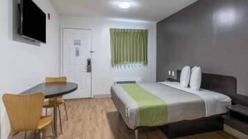 Habitación de hotel con cama, escritorio, silla, televisión y ventana con cortinas.