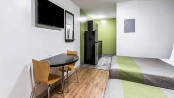 A compact room with a bed, a small table with chairs, a television mounted on the wall, and a refrigerator.