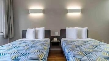 A hotel room with two beds, a nightstand, and a wall-mounted light fixture.
