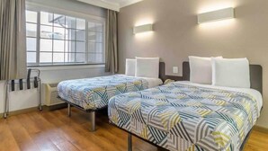 Habitación de hotel con dos camas, una ventana con cortinas, una mesita de noche con lámpara y un radiador.