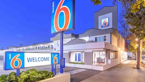 Un motel con un llamativo letrero con el número '6', un cartel de 'BIENVENIDOS' y una fachada de edificio moderna.
