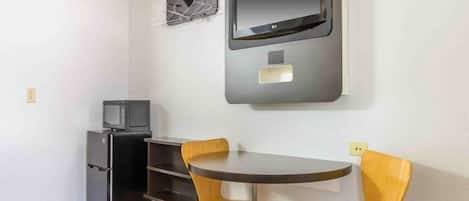 Un espacio habitable compacto con una kitchenette pequeña, un televisor de pantalla plana montado en la pared y una mesa redonda con dos sillas.