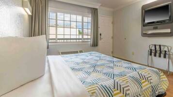 Habitación de hotel con una cama, un televisor montado en la pared y un ventanal con cortinas.