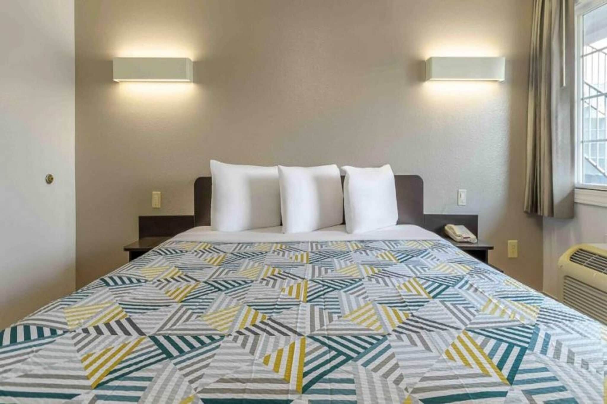 A hotel room with a bed, two bedside tables, a telephone, and a window with curtains.