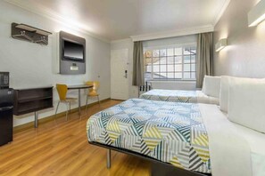 Hotellihuone, jossa on kaksi sänkyä, työpöytä, tuoli, televisio ja ikkuna, jossa on verhot.