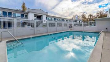 A swimming pool with a white fence, a clear blue sky, and a building with multiple windows in the background.