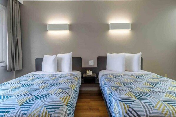 A hotel room with two beds, a nightstand, and a wall-mounted light fixture.