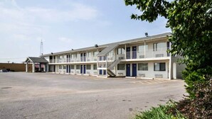 Un motel con parcheggio centrale, diverse camere dotate di balconi e un piccolo edificio adiacente.
