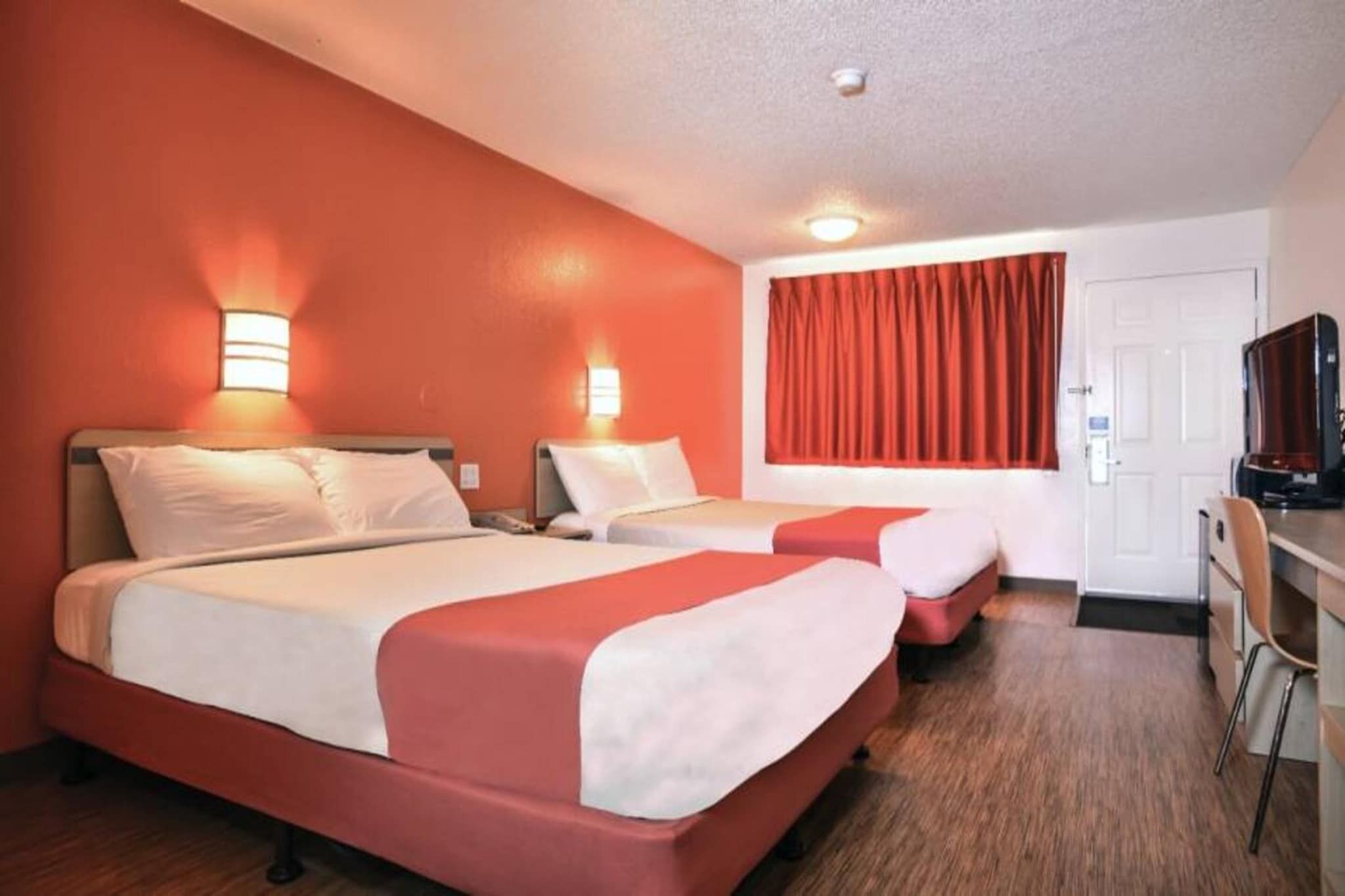 A hotel room with two beds, a desk, and a television.