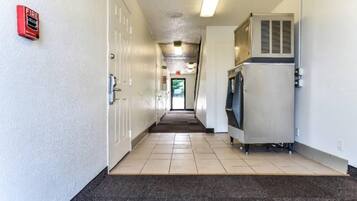 A hallway with a fire alarm on the left, a water fountain on the right, and a door at the end.