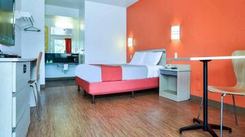 A modern hotel room with a bed, bedside table, chair, and a desk with a chair.