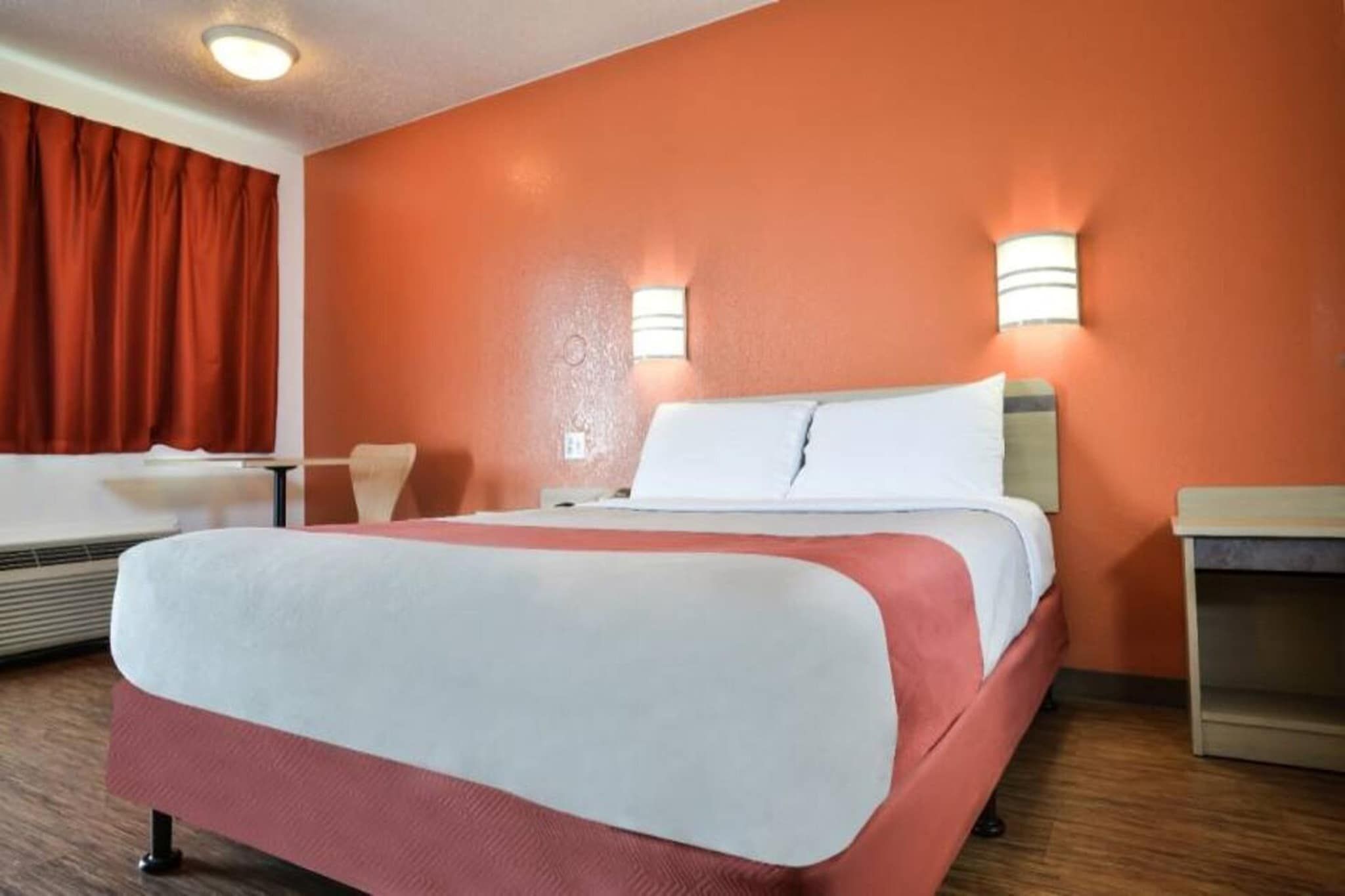 Quarto de hotel com cama, escrivaninha e cadeira.