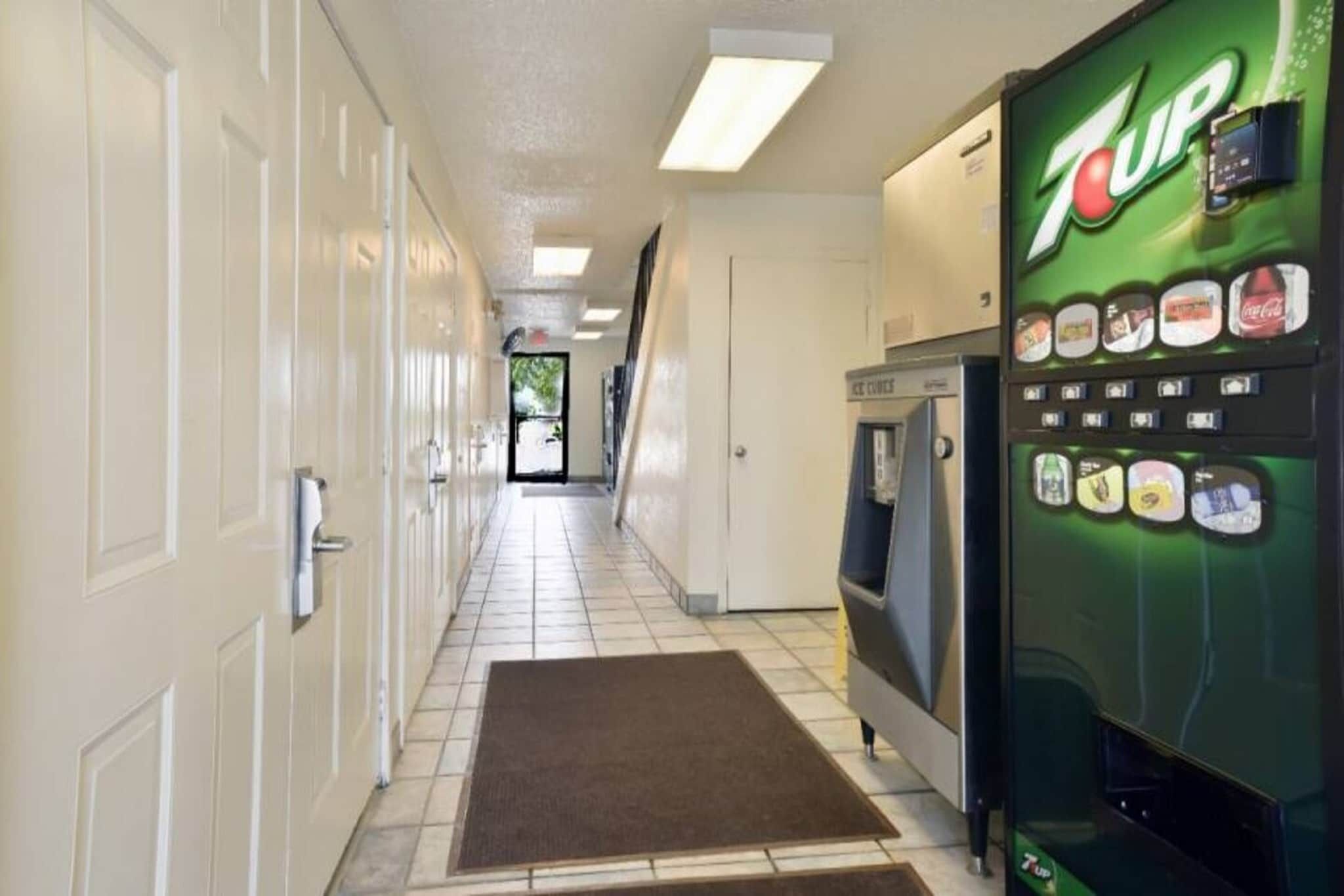 Corredor com uma máquina de refrigerantes 7UP, micro-ondas e uma porta no final.