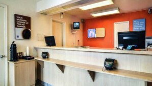 Een receptiebalie in een hotel, met een koffieapparaat, een telefoon en een televisiescherm.