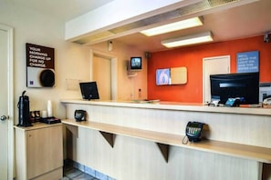 A hotel reception desk with a coffee machine, a phone, and a television screen. - 1 King Bed | ADA/RI Shower (Saint Joseph)