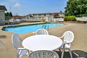 A swimming pool with a patio area, including a table and chairs, and a motel building in the background. - 1 King Bed | ADA/RI Shower (Saint Joseph)