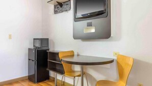 Habitación compacta con un refrigerador pequeño, un microondas, un televisor de pantalla plana montado en la pared y una mesa redonda con dos sillas.