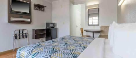 Una habitación de hotel con cama, escritorio, silla, televisor y espejo.