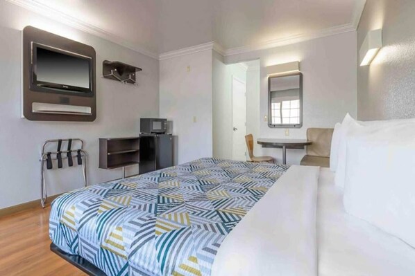 Una habitación de hotel con cama, escritorio, silla, televisor y espejo.
