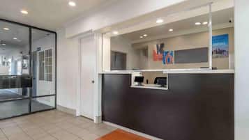 Un área de recepción con entrada por puerta de vidrio, un mostrador de recepción y suelo de baldosas.