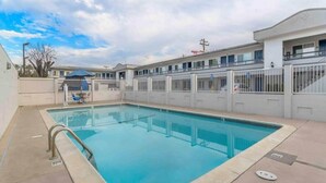 Una piscina con baranda de metal, una zona de estar cubierta y un edificio con varias ventanas y entrada protegida por un portón.