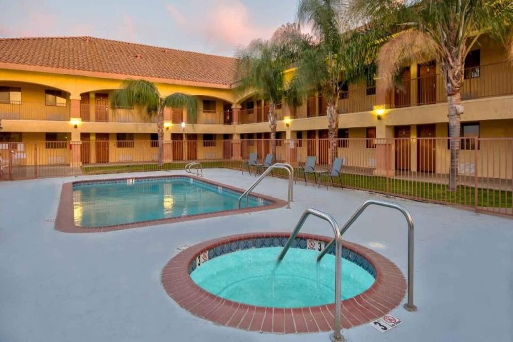 A hotel with a swimming pool, multiple balconies, and palm trees.