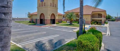 A hotel with a parking lot, palm trees, and a building with a tower.