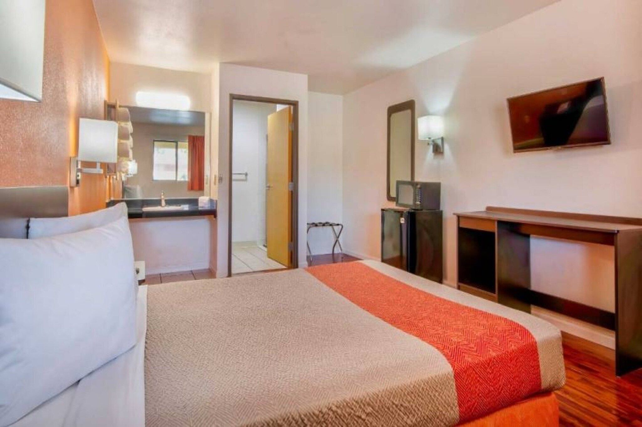 A hotel room with a bed, a desk, a television, and a kitchenette.