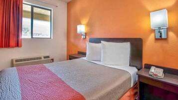 A hotel room with a bed, a heater, a window with curtains, and a wall-mounted phone.