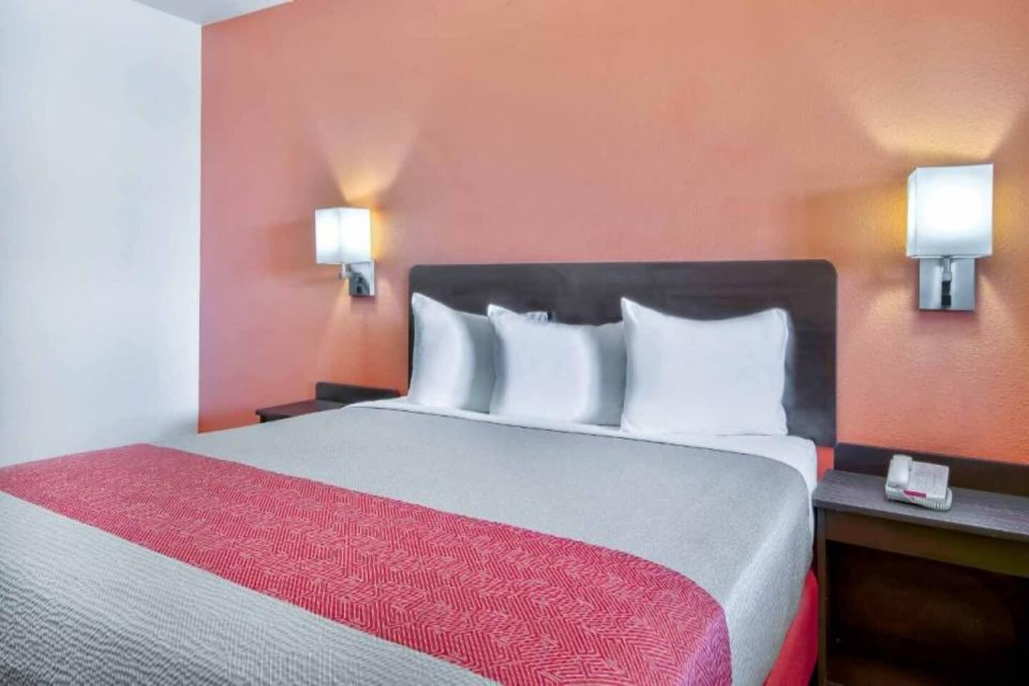 Une chambre d’hôtel avec un lit, une table de chevet et deux lampes fixées au mur.