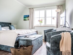 A bedroom with a bed, two armchairs, a bedside table, a lamp, a window with curtains, and a painting on the wall. - Holiday Home With 2 Bedrooms (Fuhlendorf)