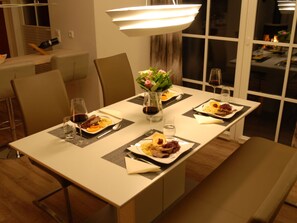 A dining area with a table set for four, including plates of food, glasses, and a vase with flowers. - Holiday Home With 2 Bedrooms (Fuhlendorf)