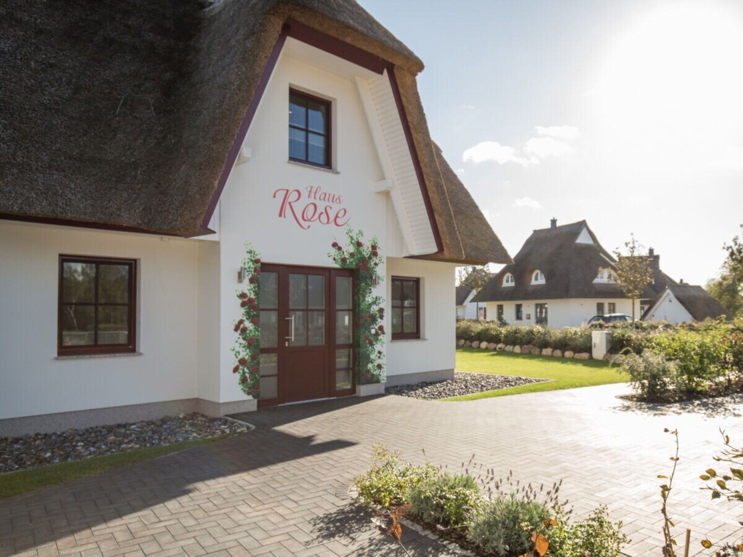 A traditional thatched-roof building with a sign reading 'Haus Rose' and a paved driveway leading to the entrance.