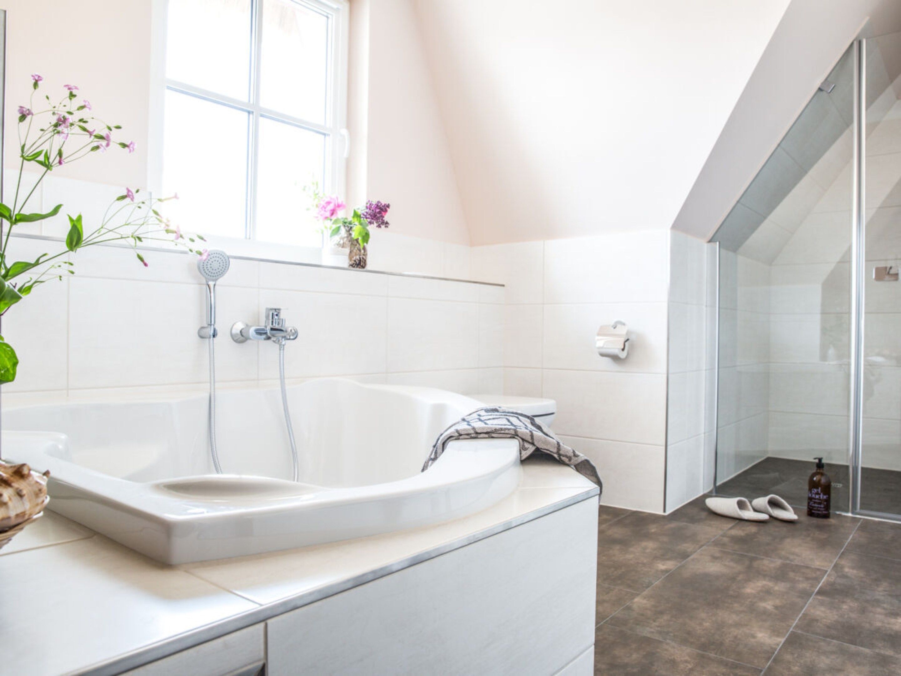 Une salle de bain moderne avec une baignoire sur pieds, une douche à parois de verre et une fenêtre laissant entrer la lumière naturelle.