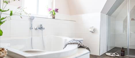 Une salle de bain moderne avec une baignoire sur pieds, une douche à parois de verre et une fenêtre laissant entrer la lumière naturelle.