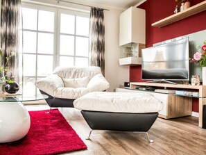 A modern living room with a sofa, ottoman, TV, and a red rug. - Holiday Home With 2 Bedrooms (Fuhlendorf)