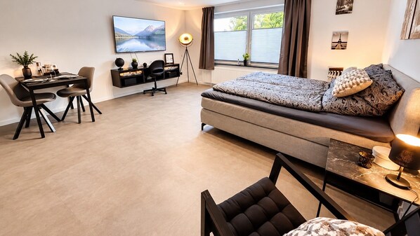 A modern living room with a sofa, a dining area with a table and chairs, a TV mounted on the wall, and a floor lamp.