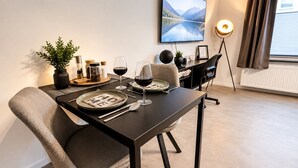 A dining area with a table set for two, a potted plant, and a framed picture on the wall.