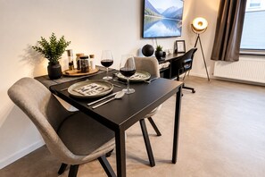 A dining area with a table set for two, a potted plant, and a framed picture on the wall.