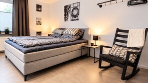 A bedroom with a bed, a chair, a nightstand, and wall art.