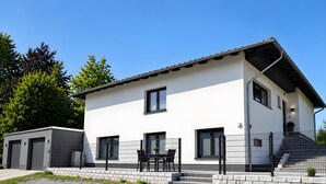 A modern two-story building with a flat roof, large windows, and a gravel driveway.
