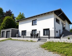 A modern two-story building with a flat roof, large windows, and a gravel driveway.