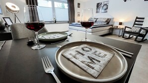 Et spisebord dækket med tallerkener, bestik og vinglas, med en sofa og stole i baggrunden.