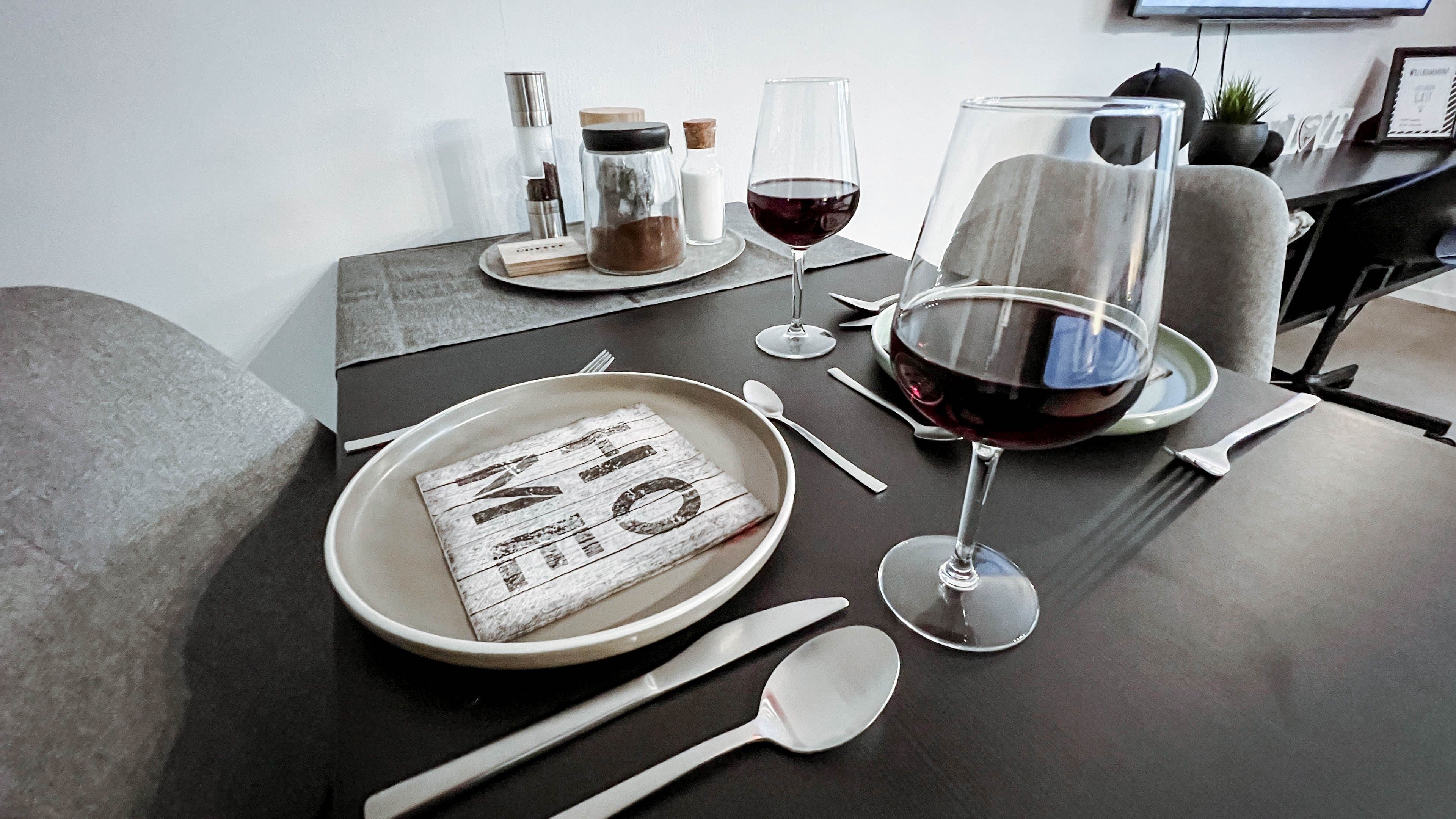A dining table set with plates, cutlery, glasses, and a bottle, indicating a meal setting.