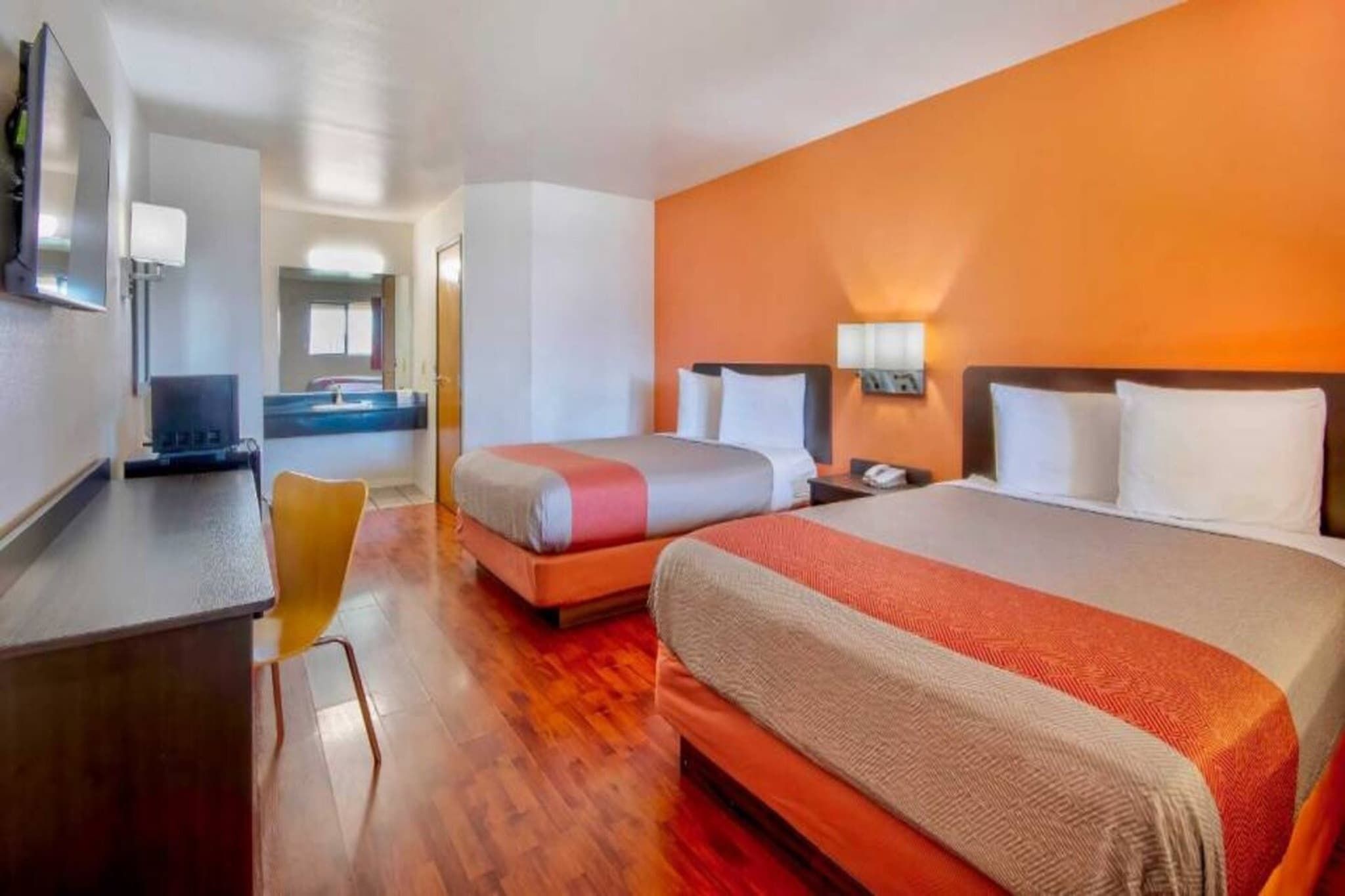 A hotel room with a bed, bedside table, and a desk with a chair.