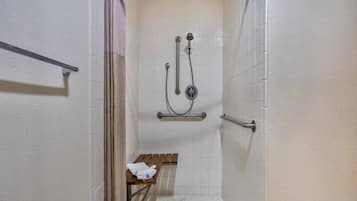 A small, enclosed shower area with a bench, a towel, and a handrail.