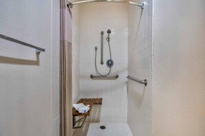 A small, enclosed shower area with a bench, a towel, and a handrail.