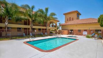 A hotel with a swimming pool, palm trees, and a building with a tiled roof.